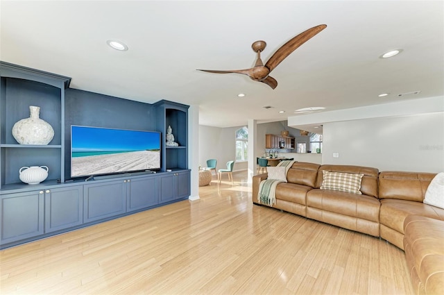 living room with built in features, light wood-type flooring, and ceiling fan