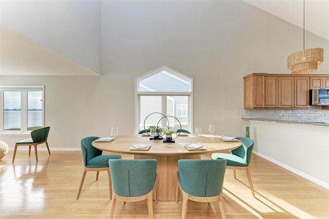 dining space with light wood-type flooring and high vaulted ceiling