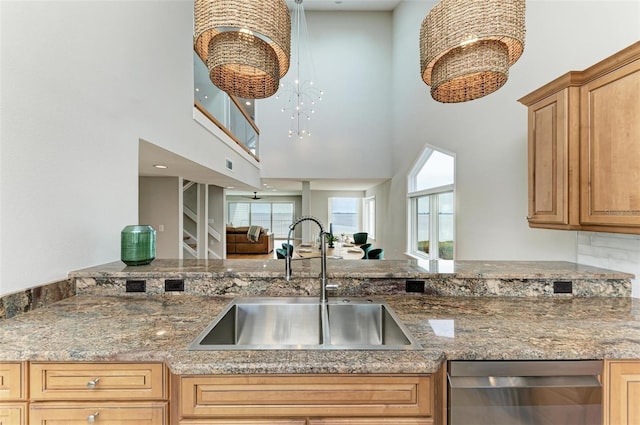 kitchen with dishwasher, sink, a high ceiling, stone counters, and a chandelier