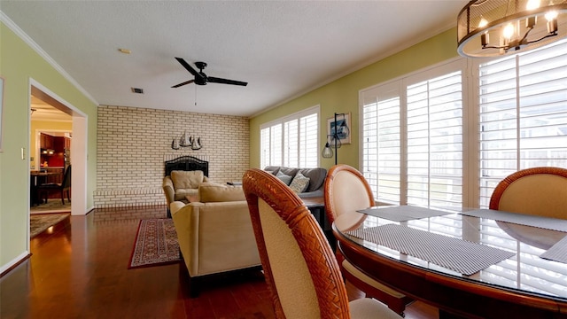 dining space featuring brick wall, a fireplace, ornamental molding, ceiling fan, and dark wood-type flooring