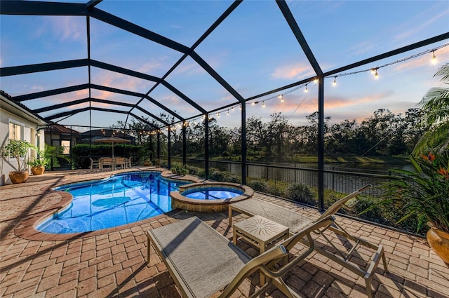 pool at dusk with an in ground hot tub, a patio, and glass enclosure