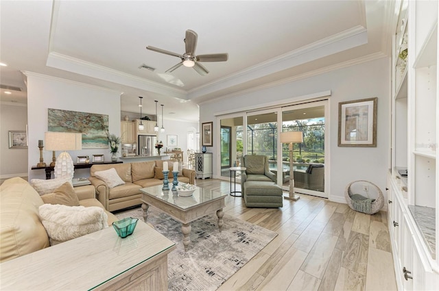 living room featuring crown molding, light hardwood / wood-style flooring, ceiling fan, and a tray ceiling