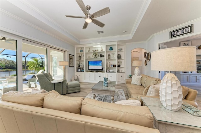 living room with crown molding, hardwood / wood-style flooring, ceiling fan, a tray ceiling, and built in shelves