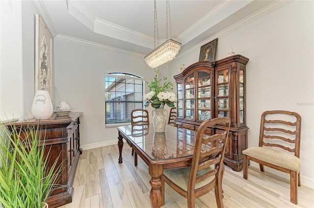 dining area with a raised ceiling, ornamental molding, and light wood-type flooring