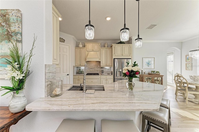 kitchen with cream cabinets, decorative light fixtures, stainless steel fridge, and a breakfast bar