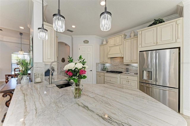 kitchen featuring pendant lighting, sink, stainless steel fridge, light stone counters, and cream cabinetry