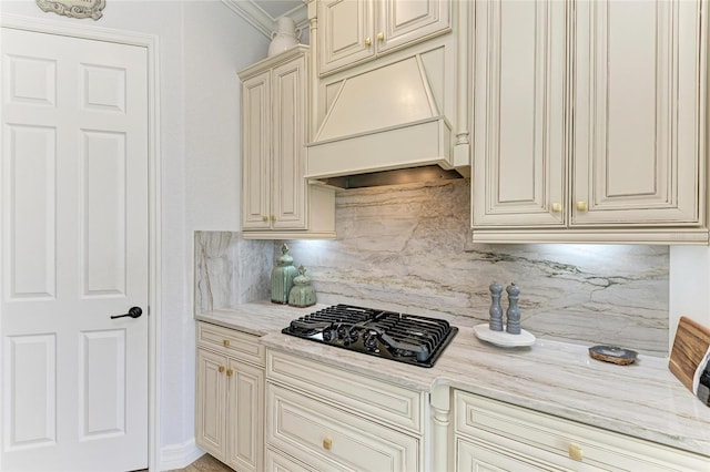 kitchen with premium range hood, black gas cooktop, tasteful backsplash, light stone counters, and cream cabinetry