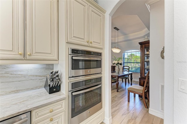 kitchen featuring crown molding, appliances with stainless steel finishes, light stone counters, cream cabinets, and tasteful backsplash