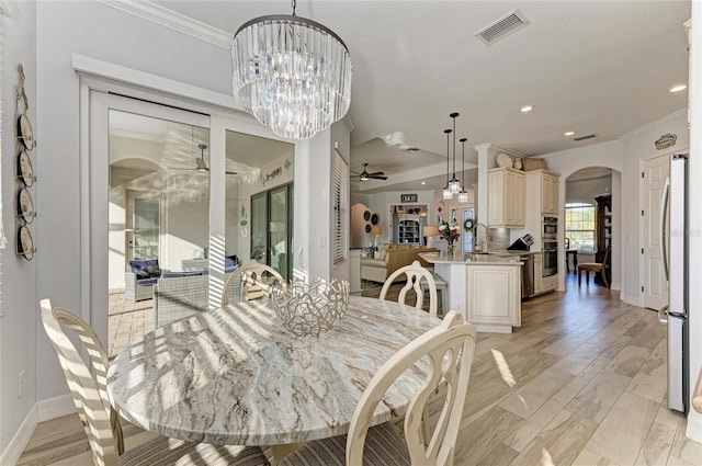 dining area with crown molding, sink, ceiling fan with notable chandelier, and light wood-type flooring