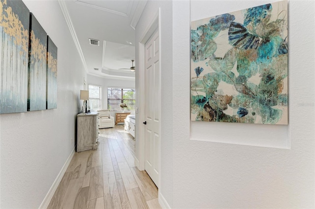 hallway with a tray ceiling, crown molding, and light wood-type flooring