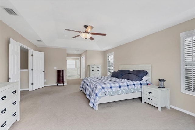 carpeted bedroom featuring a raised ceiling, connected bathroom, and ceiling fan