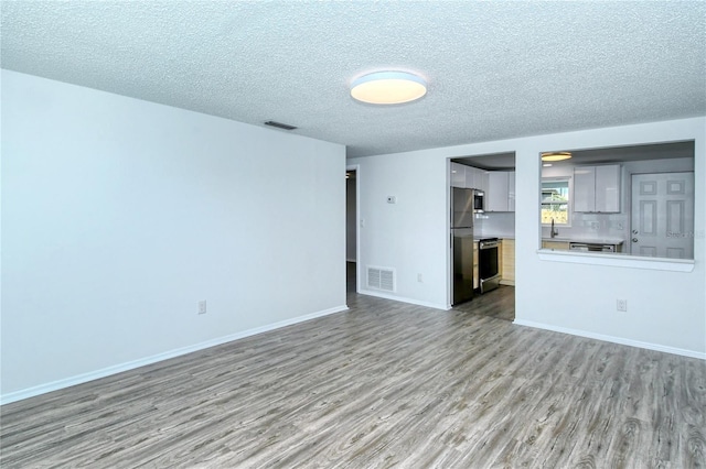 unfurnished living room with sink, light wood-type flooring, and a textured ceiling