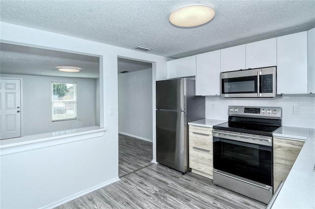 kitchen featuring white cabinetry, a textured ceiling, stainless steel appliances, and light hardwood / wood-style flooring