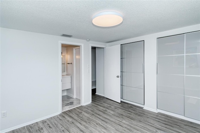 unfurnished bedroom with ensuite bath, light hardwood / wood-style flooring, multiple closets, and a textured ceiling