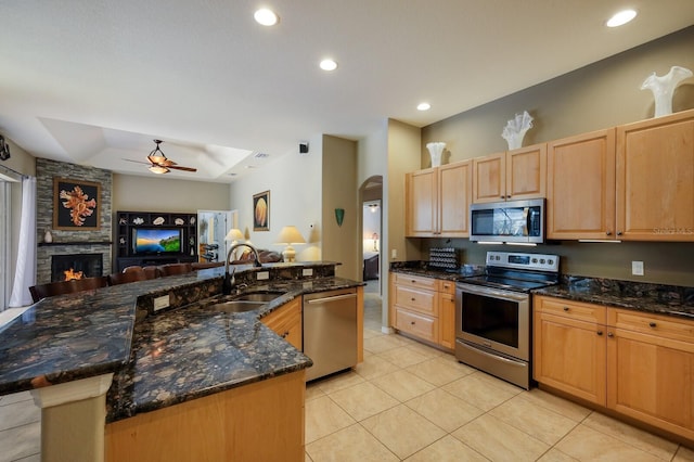 kitchen with appliances with stainless steel finishes, a fireplace, sink, dark stone counters, and a center island with sink