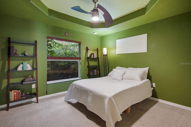 bedroom with a raised ceiling, light colored carpet, and ceiling fan