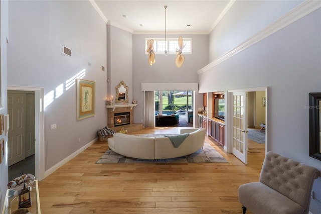 living room with a fireplace, light hardwood / wood-style floors, a towering ceiling, and ornamental molding