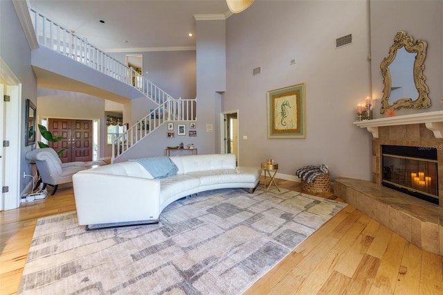 living room featuring wood-type flooring, crown molding, a towering ceiling, and a fireplace