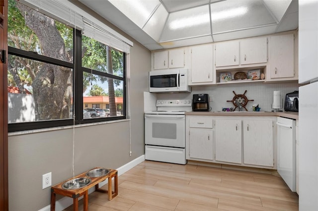 kitchen with white appliances, white cabinetry, light hardwood / wood-style floors, and tasteful backsplash