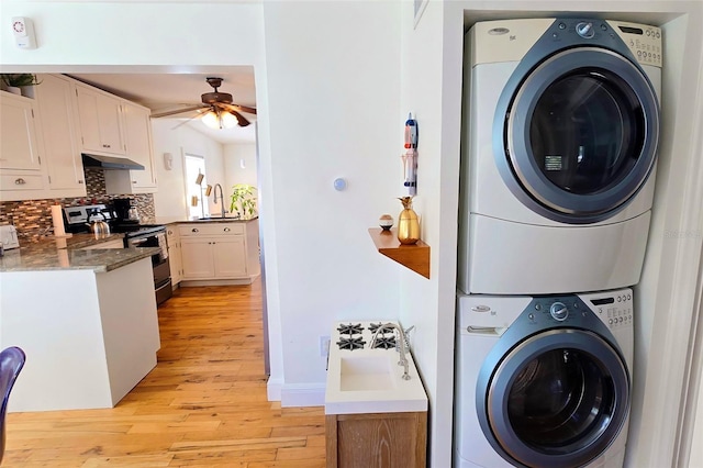 laundry room with ceiling fan, stacked washer and clothes dryer, sink, and light hardwood / wood-style flooring