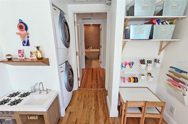 laundry room with stacked washer / drying machine, light hardwood / wood-style flooring, and sink