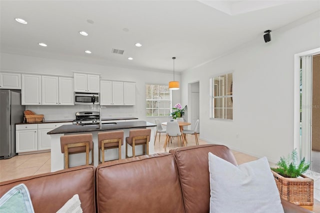 kitchen with white cabinets, stainless steel appliances, a kitchen island with sink, and pendant lighting