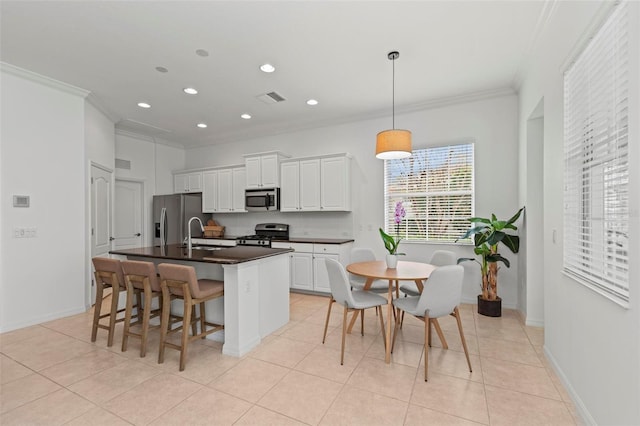 kitchen with appliances with stainless steel finishes, a kitchen island with sink, white cabinets, decorative light fixtures, and light tile patterned flooring