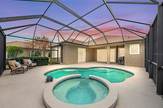 pool at dusk with an in ground hot tub, glass enclosure, and a patio area