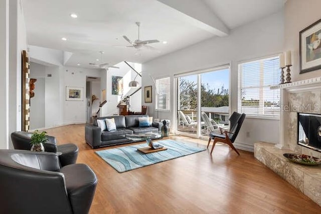 living room featuring beamed ceiling, ceiling fan, a high end fireplace, and light hardwood / wood-style floors