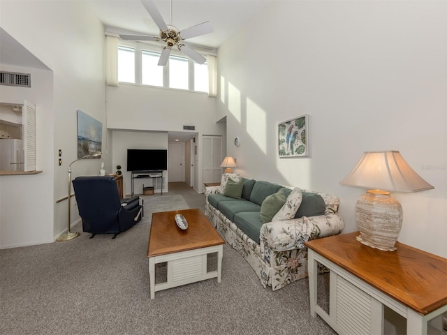 carpeted living room featuring ceiling fan and a high ceiling