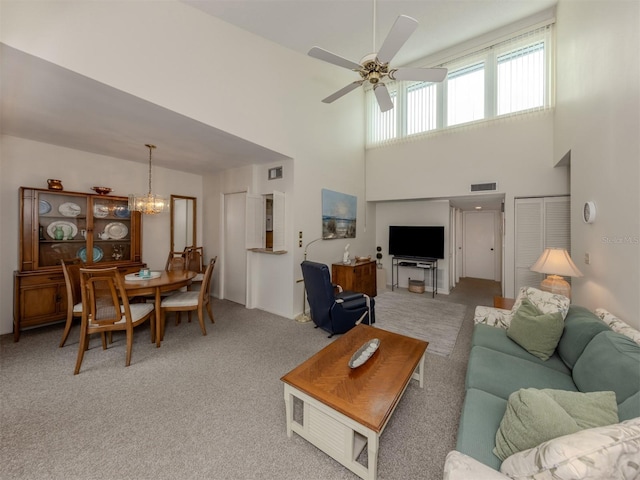 carpeted living room featuring ceiling fan with notable chandelier and a towering ceiling