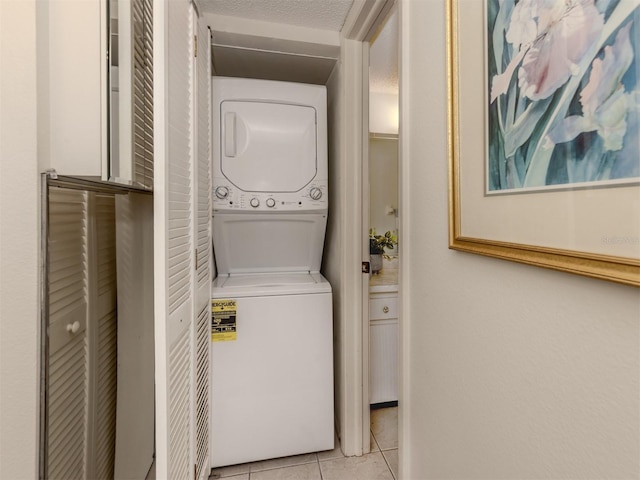 clothes washing area with stacked washer / dryer, light tile patterned floors, and a textured ceiling