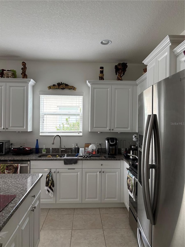 kitchen with appliances with stainless steel finishes, white cabinetry, sink, dark stone countertops, and light tile patterned floors