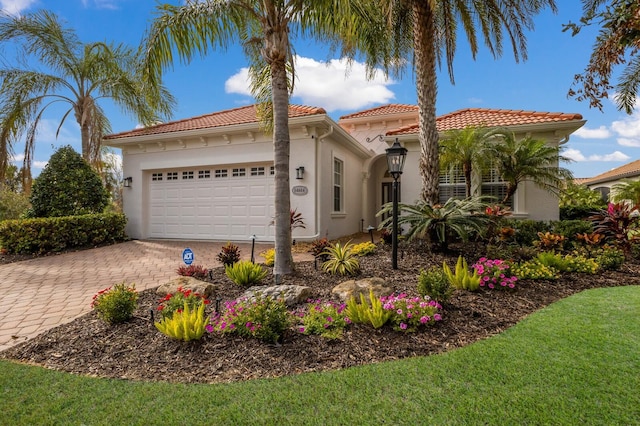 mediterranean / spanish house with decorative driveway, a tile roof, stucco siding, and an attached garage