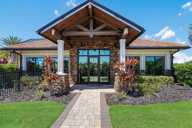 doorway to property with stone siding, fence, a tile roof, stucco siding, and french doors