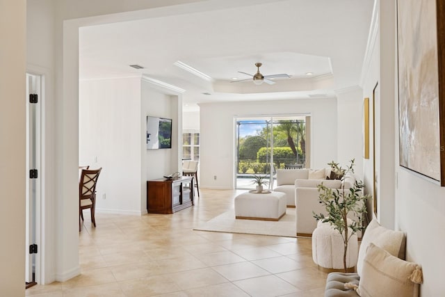 living room featuring a tray ceiling, ornamental molding, light tile patterned flooring, visible vents, and a ceiling fan