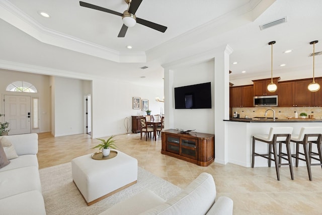 living area with ceiling fan, visible vents, ornamental molding, and a raised ceiling