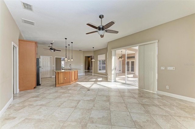 kitchen featuring sink, a center island with sink, stainless steel refrigerator, pendant lighting, and ceiling fan