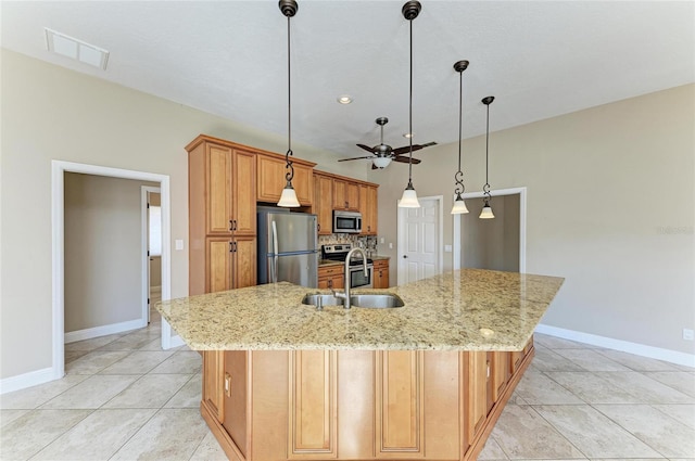 kitchen featuring pendant lighting, sink, a large island with sink, stainless steel appliances, and light stone countertops