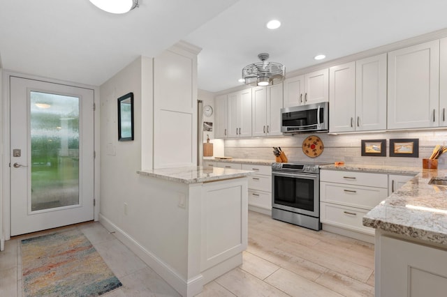 kitchen with white cabinetry, tasteful backsplash, appliances with stainless steel finishes, kitchen peninsula, and light stone countertops