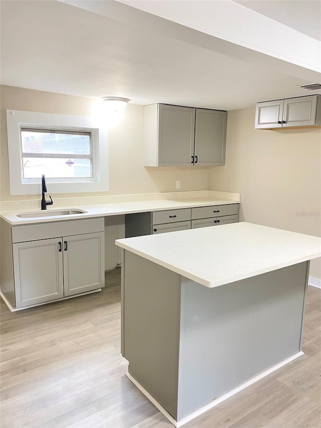 kitchen with sink, gray cabinetry, a kitchen island, and light hardwood / wood-style flooring