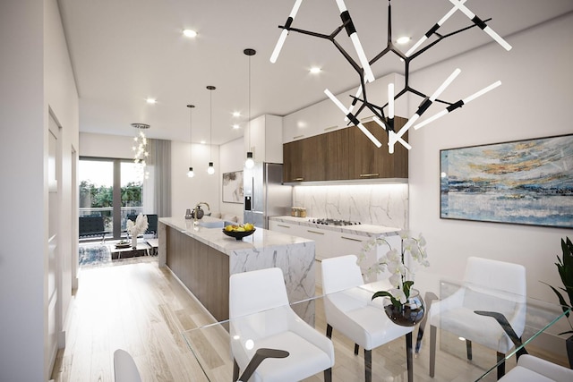 kitchen featuring hanging light fixtures, appliances with stainless steel finishes, white cabinets, an island with sink, and decorative backsplash