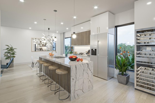 kitchen with white cabinetry, a kitchen breakfast bar, hanging light fixtures, light stone counters, and a center island with sink