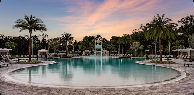 pool at dusk with a gazebo, a water slide, a patio area, and a community pool