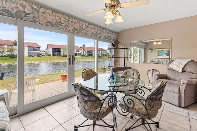 dining room featuring ceiling fan, a water view, light tile patterned floors, and a textured ceiling