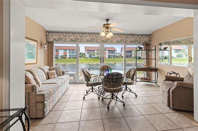 tiled dining area with ceiling fan, a textured ceiling, and a water view