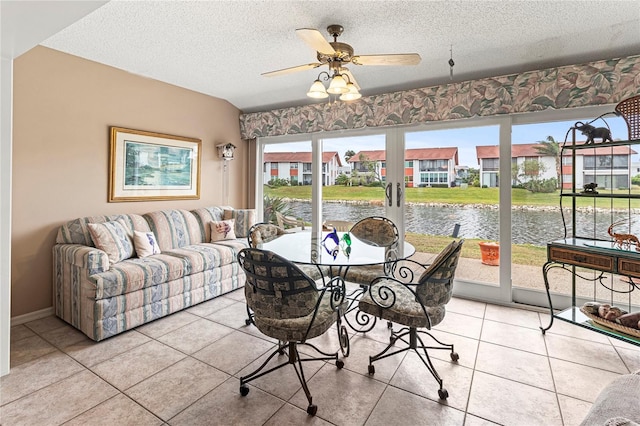 tiled dining room featuring ceiling fan, a textured ceiling, and a water view