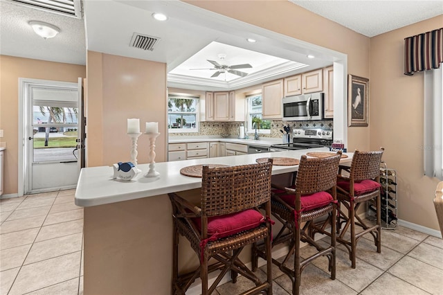 kitchen featuring stainless steel appliances, a kitchen bar, a tray ceiling, and light tile patterned floors