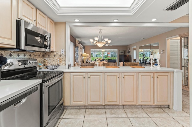 kitchen with ornamental molding, appliances with stainless steel finishes, kitchen peninsula, a notable chandelier, and decorative backsplash