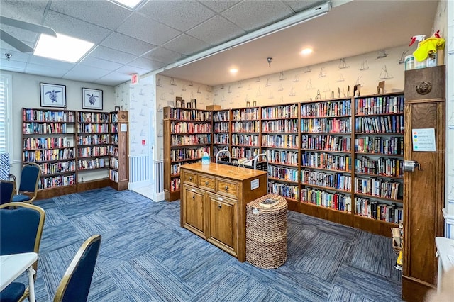 living area featuring carpet floors, baseboards, wall of books, and wallpapered walls